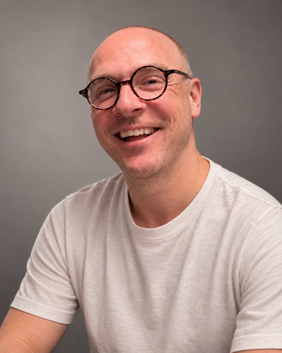 James Nicholson, smiling, in round tortoiseshell glasses and a white T-shirt.
